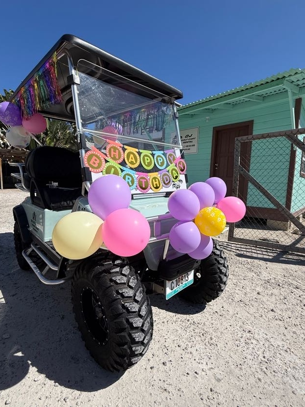 Teal golf cart decorated with colorful Happy Birthday banner and purple pink yellow balloon clusters in San Pedro Belize